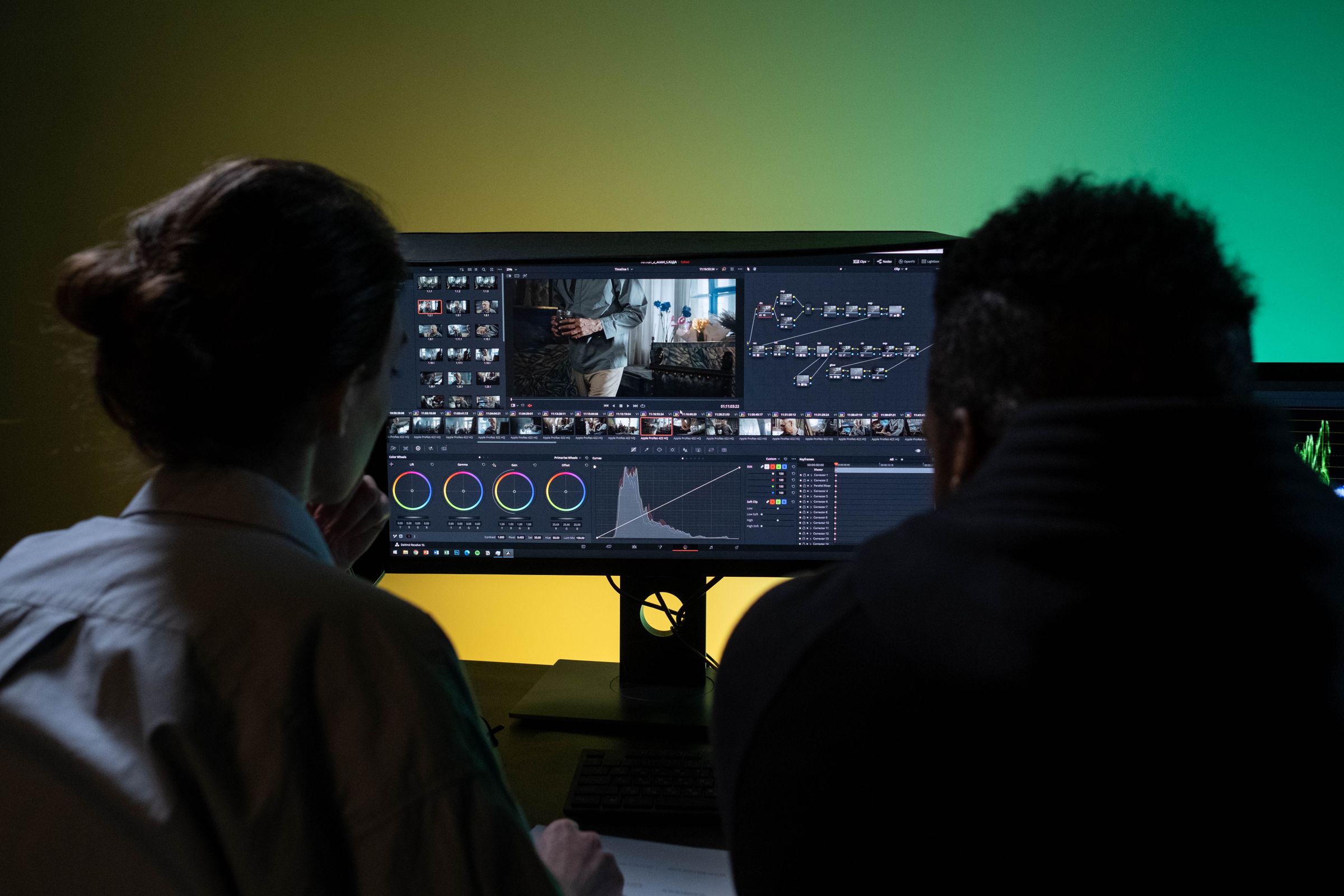 Two people editing video at a dual-monitor workstation.